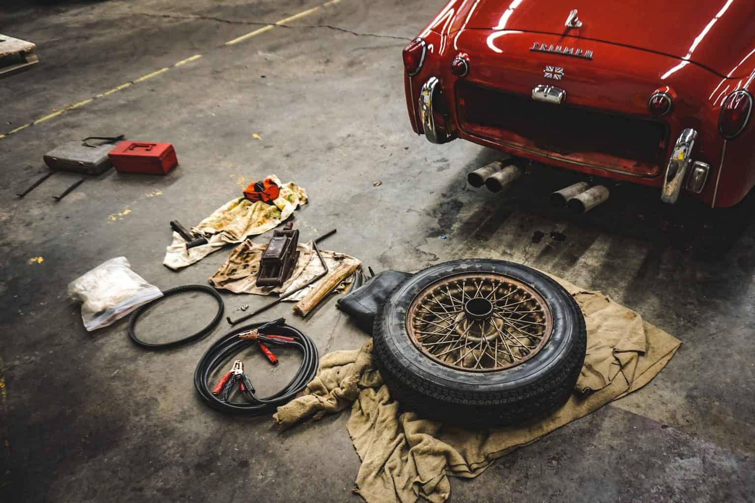 Different kinds of tools and a wheel behind the red car