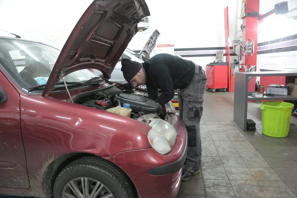 A person inspecting an engine of a red car