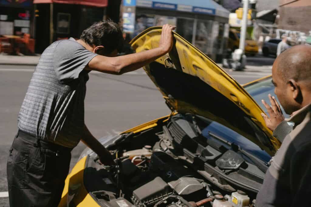 Two people checking a car engine of a yellow car in a sunny day